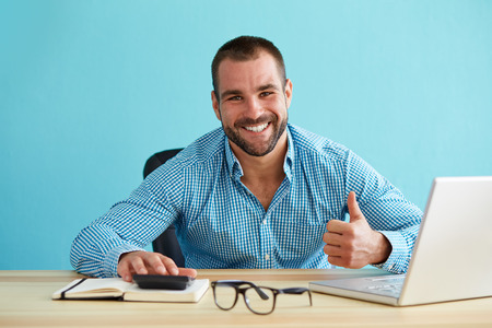 Smiling businessman calculates taxes and gestures with a thumbs up to portray the concept of tax credits.